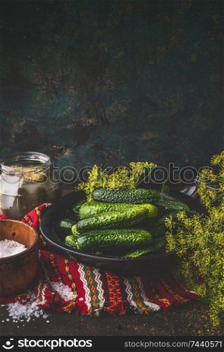 Close up of fresh cucumber in bowl with dill, herbs and spices for pickling and preserving on dark rustic kitchen table. Healthy fermented food concept. Harvest storing . Still life