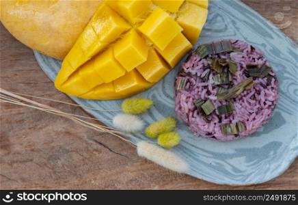Close-up of Fresh ripe yellow mango fruit (Barracuda mango) and Riceberry topping pandan leaf on ceramic plate. Selective focus.