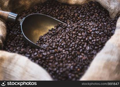 Close-up of freshly roasted Arabica coffee beans with an aged scoop in a jute bag. Coffee beans in open sack. Roasted black coffee beans background.