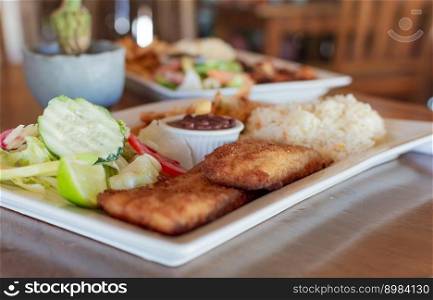 Close up of fried fish fillet with rice and salad served on table with copy space. Gourmet food fried fish fillet with salad rice served on wooden table, gourmet food fried fish fillet