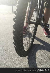 Close up of front bike wheel on asphalt and male legs. Close up of bike wheel