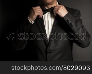Close-up of gentleman wearing black tie straightens his bowtie on black