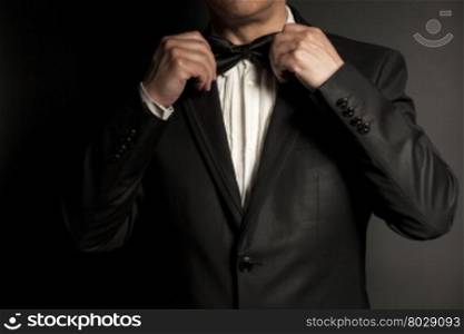 Close-up of gentleman wearing black tie straightens his bowtie on black