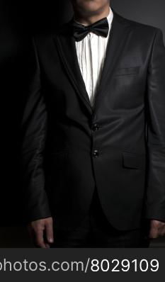 Close-up of gentleman wearing black tie straightens his bowtie on black