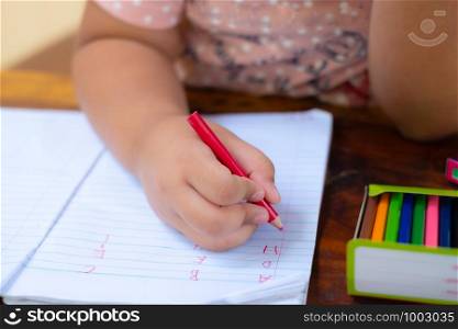Close up of girl hand with pencil writing english words by hand on white notepad paper at white background, Child learning to write letters of the alphabet, A child is holding a crayon in his hands at paper and crayons for drawing