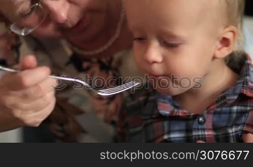 Close up of grandmother feeding her cute little grandson with organic food at the table during celebrating Thanksgiving family reunion at home.