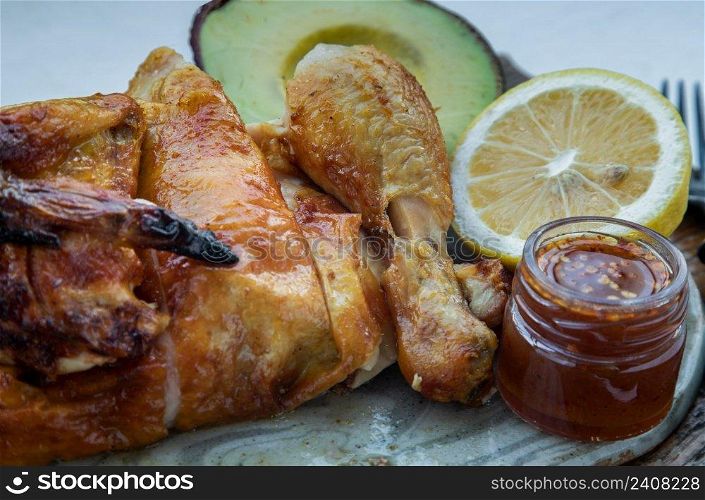 Close-up of Grilled chicken or Roasted chicken with Avocado and Lemon cut in half serve with Sweet chili sauce. Healthy thai food concept, Selective focus.