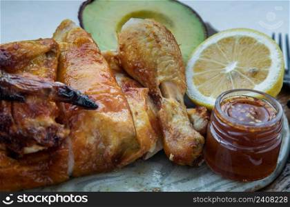 Close-up of Grilled chicken or Roasted chicken with Avocado and Lemon cut in half serve with Sweet chili sauce. Healthy thai food concept, Selective focus.