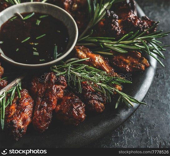 Close up of grilled chicken wings with rosemary and flavorful barbecue sauce on dark background.  Ready to eat. Front view.