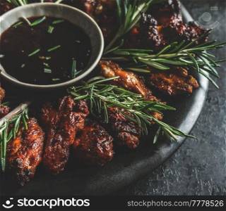 Close up of grilled chicken wings with rosemary and flavorful barbecue sauce on dark background.  Ready to eat. Front view.