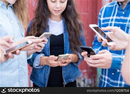 Close Up Of Group Of Teenage Friends Looking At Mobile Phones In Urban Setting