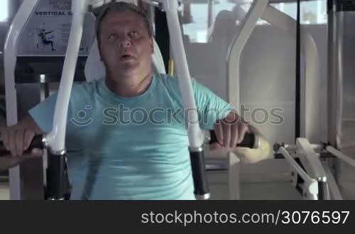 Close-up of grown man in gym sitting on the exerciser and performs exercises chest press and then resting