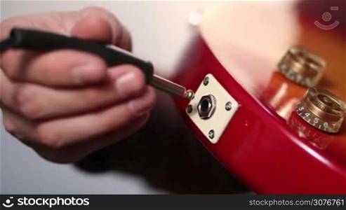 Close up of guitarist hand plugging in instrument cable into the jack input of red electric guitar. Detail of red electric guitar with cord plugging into the jack.