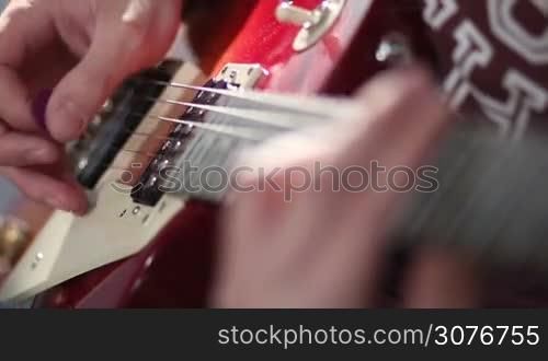 Close up of guitarist hands playing on red electric guitar using tremolo technique during jamming in studio.