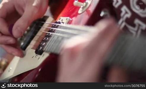 Close up of guitarist hands playing on red electric guitar using tremolo technique during jamming in studio.