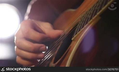 Close up of guitarist male hand and fingers touching acoustic six string guitar strings. Musician performing chords on acoustic guitar.