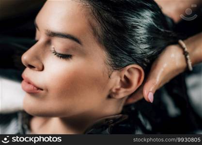 Close-up of hairdresser’s hands washing woman’s hair.. Young Woman Having Hair Washed in Salon