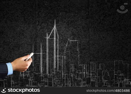 Close up of hand drawing urban city building on chalk board. Development project