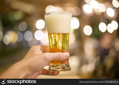 Close up of hand holding a glass of beer to celebrate at restaurant.