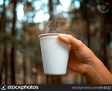 Close-up of hand holding hot beverage in paper glass in the morning on blur nature background. Relaxation travel concept.