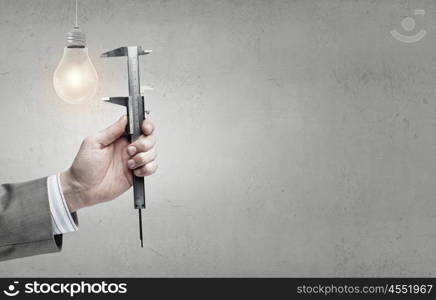 Close up of hand measuring light bulb with wrench. Measure it up