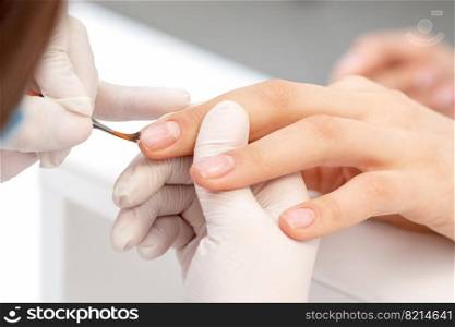 Close up of hand of manicurist applying clear nail polish in beauty salon.. Hand of manicurist applying clear nail polish