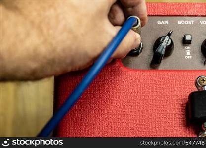 Close up of hand plugging in jack on panel of red electric guitar amplifier