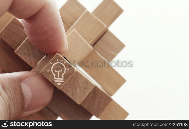 close up of hand showing illuminated light bulb icon on a wooden block puzzle as innovation concept