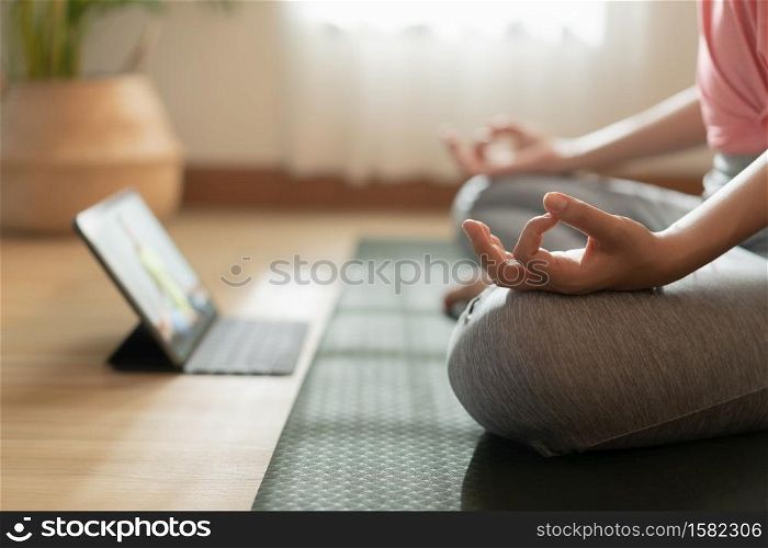 Close up of hand woman doing lotus yoga exercises on yoga mat with Training online on the tablet at home morning, Concept of relaxation and meditation