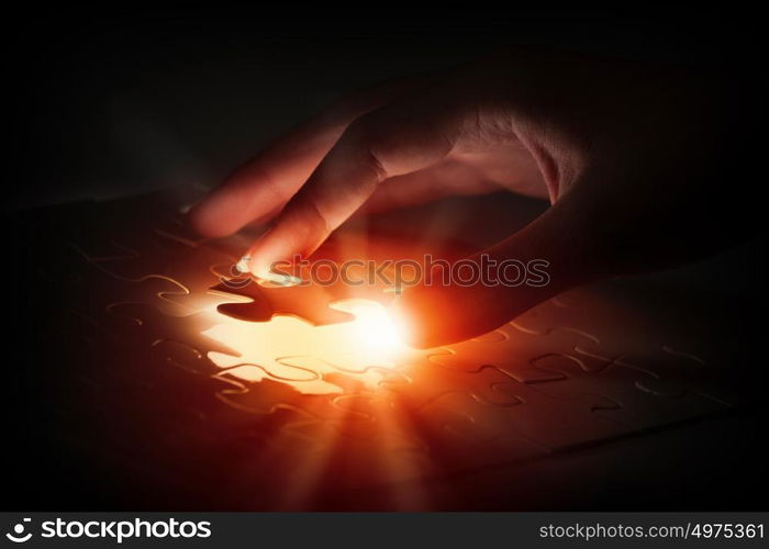 Close up of hands connecting puzzle element and making jigsaw complete. Jigsaw game