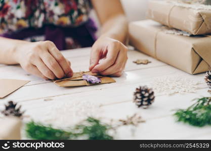 Close up of hands holding wrapping gift box and christmas card on wooden table with xmas decoration.