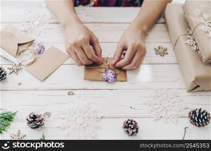 Close up of hands holding wrapping gift box and christmas card on wooden table with xmas decoration.