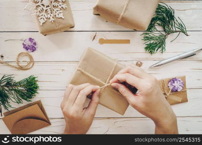 Close up of hands holding wrapping gift box on wooden table with xmas decoration.