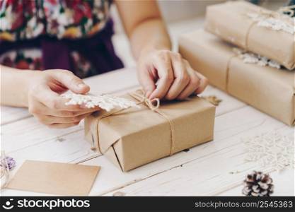 Close up of hands holding wrapping gift box on wooden table with xmas decoration.