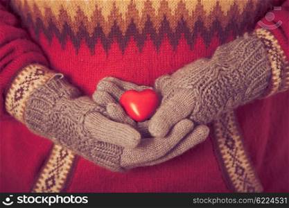 Close-up of hands in grey knitted mittens holding red heart. Valentine day concept