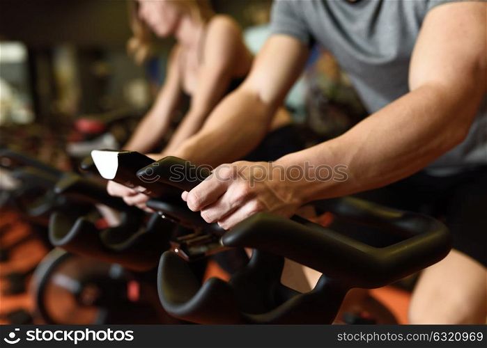 Close-up of hands of a man biking in the gym, exercising legs doing cardio workout cycling bikes. Couple in a spinning class wearing sportswear.