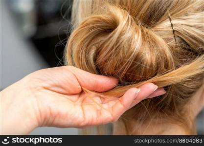 Close up of hands of female hairdresser styling hair of a blonde woman in a hair salon. Hairdresser styling hair of woman