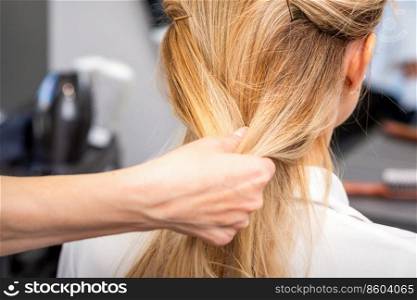Close up of hands of female hairdresser styling hair of a blonde woman in a hair salon. Hairdresser styling hair of woman