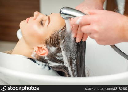 Close up of hands of hairdresser washing hair of woman in sink at beauty salon. Hands of hairdresser washing hair of woman