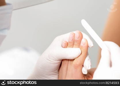 Close up of hands of manicure master doing manicure procedure by nail file.. Manicure procedure by nail file.