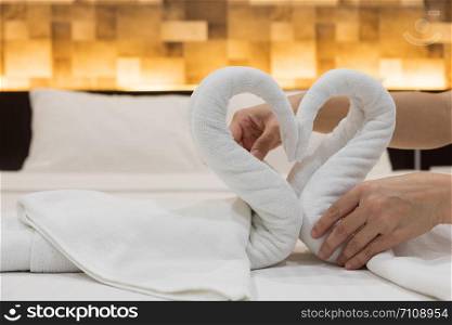 Close-up of hands putting folded swans bird of fresh white bath towels on the bed sheet in the hotel.