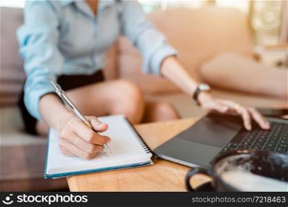 Close-up of hands Taking written Notes to on notebook and freelance business female casual working with laptop computer ,warm milk cup in coffee shop like,Distance job communication concept