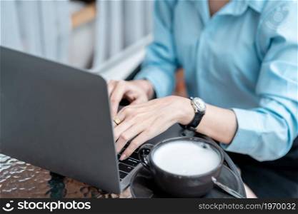 Close-up of hands typing of freelance business female casual working with laptop computer and Taking written Notes to on notebook,warm milk cup in coffee shop like,Distance job communication concept