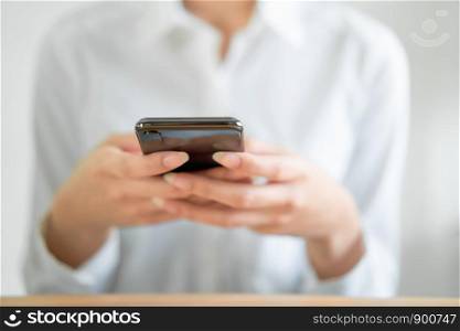 Close-up of hands using smartphone on wooden table and typing message to his friends.