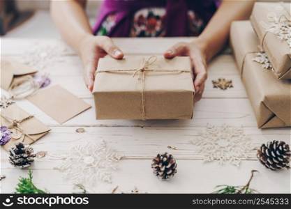 Close up of hands woman present gift box on wooden table with xmas decoration.