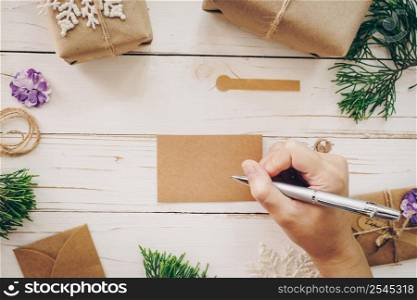 Close up of hands woman writing empty wishlist and christmas card on wooden table with xmas decoration.