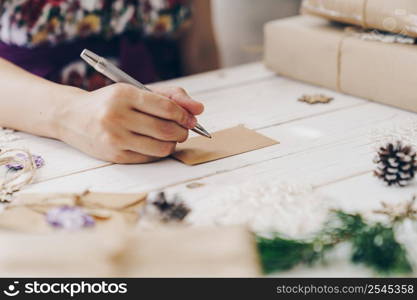 Close up of hands woman writing empty wishlist and christmas card on wooden table with xmas decoration.