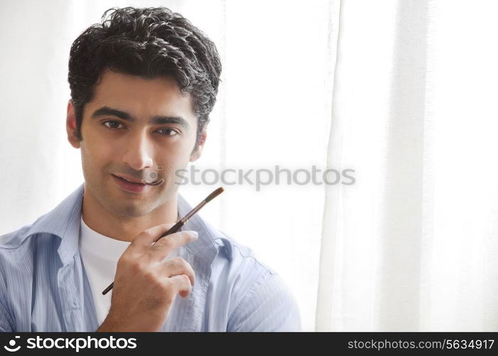 Close-up of handsome young man holding paintbrush in art studio