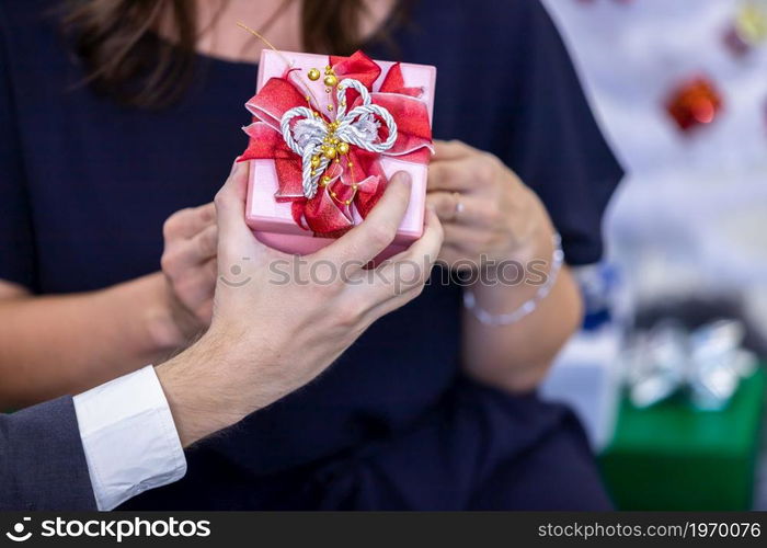 Close up of Happy couple of wrist in a business suit holding exchanging gift box and Give a present in Christmas and New Year&rsquo;s Eve party Christmas tree After finishing business work