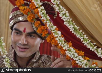 Close-up of happy Indian bridegroom behind wreath looking away